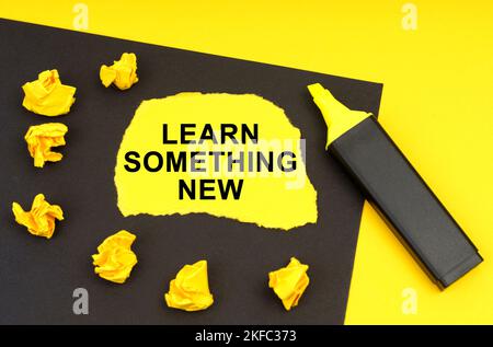 Concept d'entreprise et d'éducation. Sur fond jaune, une feuille noire sur laquelle repose le papier jaune avec l'inscription - apprendre quelque chose de nouveau Banque D'Images