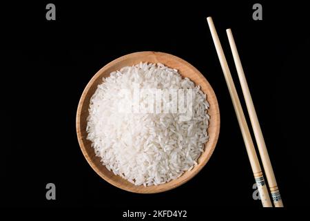 Riz blanc cru et baguettes sur fond noir. Riz long non cuit dans une assiette en bois. Nourriture biologique naturelle. Culture traditionnelle asiatique des céréales. Banque D'Images