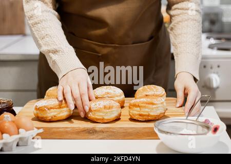 La femme prépare des beignets frais avec de la confiture dans la cuisine.Cuisine traditionnelle juive Hanoukkah sufganiyot.Saupoudrer les mains de Berliners de sucre en poudre. Banque D'Images