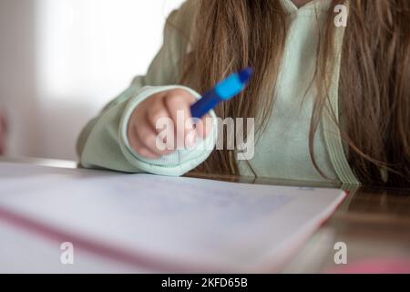 Devoirs.Schoolgirl fait ses devoirs. l'enfant écrit avec un crayon dans un bloc-notes. crayon dans une main d'enfant. Banque D'Images