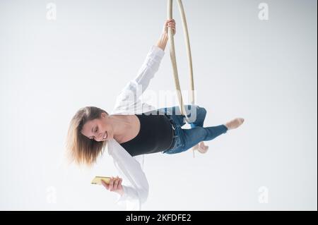 Gymnaste caucasien de sexe féminin faisant des exercices de canulars aériens et en utilisant un smartphone. Banque D'Images