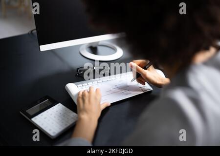 Une femme africaine signant un chèque de banque ou un chèque de paie Banque D'Images