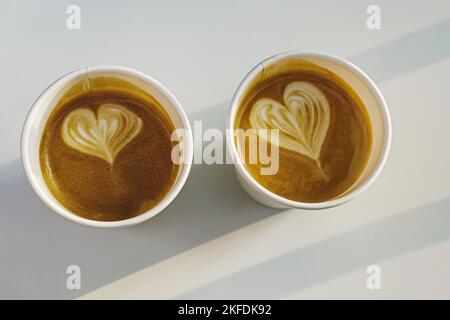 Deux tasses en papier de café avec coeurs dessinés sur la table blanche, vue du dessus. Lumière naturelle du soleil Banque D'Images