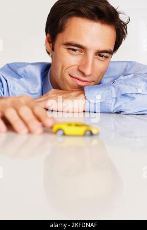 Homme jouant avec une voiture-jouet pensant à une nouvelle stratégie commerciale. Homme d'affaires jouant avec une voiture de jouet jaune pensant à la nouvelle stratégie d'affaires. Banque D'Images