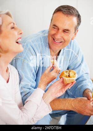 Bonne humeur femme mûre nourrissant un muffin à son mari. Portrait d'une femme mûre et gaie qui nourrit son mari de muffin. Banque D'Images