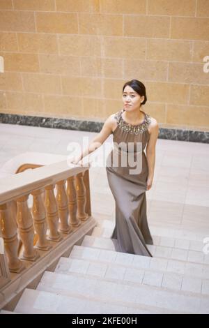 Croissant avec poise. Portrait d'une jeune femme élégamment habillée debout sur un escalier. Banque D'Images