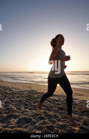 Maintien de la forme dans un environnement magnifique. Silhouette d'une jeune femme qui court sur la plage au coucher du soleil. Banque D'Images