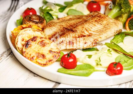 Gros plan de poissons et légumes de mer frits. Filet de tilapia au brocoli, tomates cerises et laitue. Fruits de mer sur une assiette blanche Banque D'Images