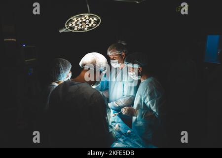 Une équipe professionnelle internationale de chirurgien, d'assistants et d'anesthésiste effectue une opération complexe sur un patient sous anesthésie générale. Sombre Banque D'Images