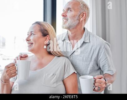 Couple âgé, câlin et café par fenêtre avec le sourire dans la contemplation, la vision ou la routine matinale à la maison. Homme et femme heureux, souriant Banque D'Images