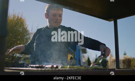 L'homme adulte cuit sur le gril, retournez les légumes, montre jusqu'au point de vente, sourit et engage votre travail préféré. Week-end sur le marché agricole local. Agriculture. Banque D'Images