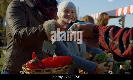 Les conjoints magasinent sur le marché agricole local. La femme se tient avec un panier de fruits ou de légumes. Le mari paie l'achat sans contact. Plats végétariens et bio. Agriculture. Vue rapprochée. Banque D'Images