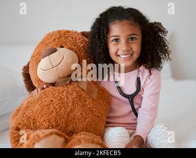 Stéthoscope, ours en peluche et fille avec un enfant son animal bourré avec un sourire dans sa maison. Portrait d'une jeune femme heureuse tenant un jouet moelleux Banque D'Images