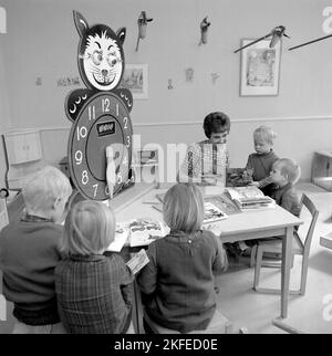 Dans le 1960s. Le centre commercial et la région de Farsta Centrum offrent aux clients parents un service de recherche de leurs enfants tout en faisant le shopping. Photo de quatre enfants avec une femme à une table de lecture et de jeu. Une horloge d'apprentissage est visible, avec des chiffres très grands pendant des heures pour que les enfants puissent jouer et apprendre avec. Suède 1967. Conard réf. 5427 Banque D'Images