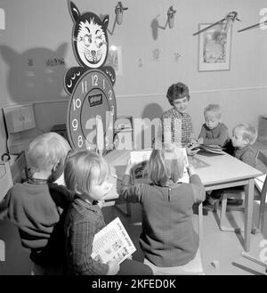 Dans le 1960s. Le centre commercial et la région de Farsta Centrum offrent aux clients parents un service de recherche de leurs enfants tout en faisant le shopping. Photo de quatre enfants avec une femme à une table de lecture et de jeu. Une horloge d'apprentissage est visible, avec des chiffres très grands pendant des heures pour que les enfants puissent jouer et apprendre avec. Suède 1967. Conard réf. 5427 Banque D'Images