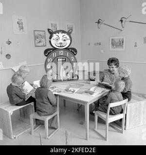 Dans le 1960s. Le centre commercial et la région de Farsta Centrum offrent aux clients parents un service de recherche de leurs enfants tout en faisant le shopping. Photo de quatre enfants avec une femme à une table de lecture et de jeu. Une horloge d'apprentissage est visible, avec des chiffres très grands pendant des heures pour que les enfants puissent jouer et apprendre avec. Suède 1967. Conard réf. 5427 Banque D'Images