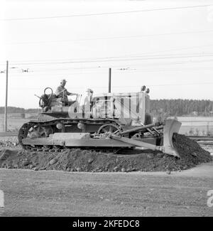 Dans le 1950s. La machinerie lourde, un bulldozer a l'air gigantesque en comparaison avec l'homme hte assis dans le siège du conducteur avec la cabine ou la protection autour de lui. Il s'agit d'un moteur diesel Caterpillar de 20 tonnes de D7 ch et de 240 ch. Cat est le plus court pour Caterpillar. La photo est prise sur un chantier de construction de chemin de fer lorsque le bulldozer aplatit et répartit le matériau utilisé pour poser les voies ferrées. Suède août 1955 Banque D'Images