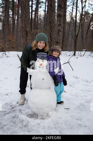 une fille adulte et un petit garçon s'amusent sur une promenade d'hiver, fait un bonhomme de neige. Des émotions de joie et de plaisir. Séjour en famille dans la forêt enneigée. Enfant intéressant Banque D'Images