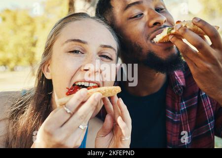 Pizza, amour et heureux couple de manger rapidement pendant un rendez-vous ensemble dans la nature dans un jardin. Faim, nourriture et portrait d'un homme et d'une femme interraciaux Banque D'Images