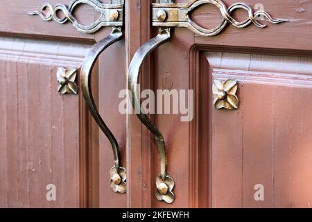 Porte d'entrée en bois marron avec poignées en métal forgé plaqué or et extérieur orné. Banque D'Images