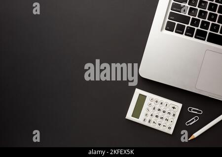 Table de travail noire avec ordinateur portable, calculatrice, crayon et trombones. Espace pour votre inscription. Banque D'Images
