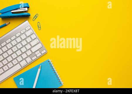 Table jaune de travail avec clavier, ordinateur portable, crayon, agrafeuse et trombones. Espace pour votre inscription. Banque D'Images