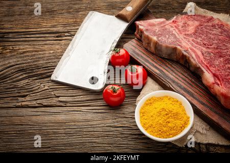 Steaks de bœuf crus sur l'os avec une hache, une tomate cerise et des épices.