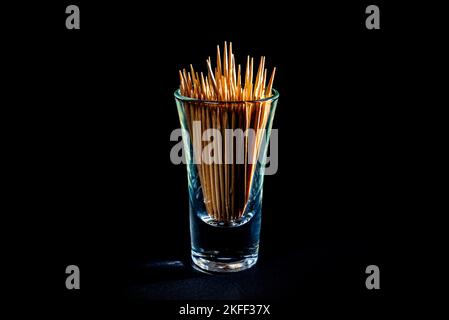 cure-dents en bois de bambou dans un pot en verre, verre à vin. dans un seau. cure-dents sur fond noir. vue de face cure-dents, déposés à la main, place pour le texte Banque D'Images