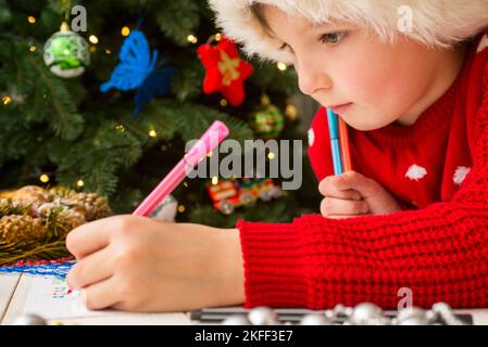 Petit garçon à Santa Hat écrit la lettre au Père Noël Banque D'Images