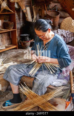 Une femme thaïlandaise âgée se tissage dans sa chaise montrant un groupe de tournée comment elle fabrique son produit. Banque D'Images