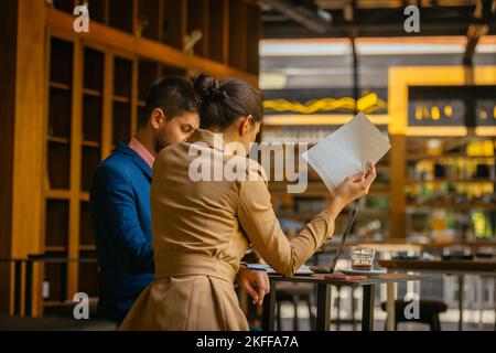 Deux beaux hommes d'affaires travaillent sérieusement sur leur projet, assis dans un café bar, un jour ensoleillé Banque D'Images