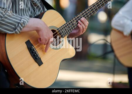 Homme jouant de la guitare basse acoustique lors d'un événement en plein air, vue rapprochée du cou de guitare en bois. Joueur de basse droitier homme jouant quatre cordes guitare basse, Banque D'Images