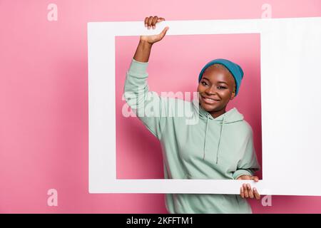 Portrait d'une jeune fille adorable tenant un grand cadre polaroid blanc image d'elle-même isolée sur fond rose couleur Banque D'Images