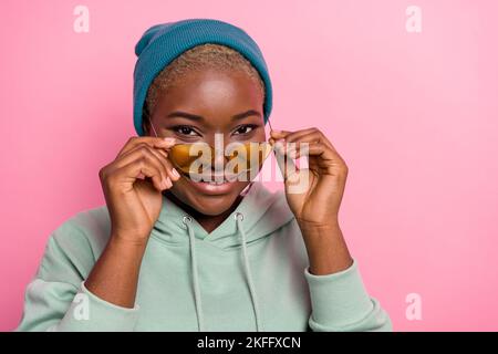 Photo d'une jolie fille à la mode dans un bonnet et un verre de soleil frais regardez votre appareil photo isolé sur fond de couleur rose Banque D'Images