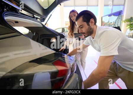 Le client de la concession automobile inspecte le coffre à bagages sous la supervision d'une femme de vente Banque D'Images
