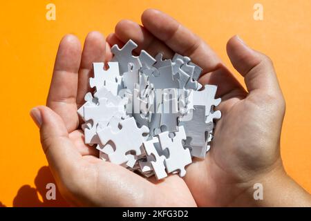 Pièces de puzzle blanches dans les mains sur fond orange. Concept de jeu de société. Banque D'Images