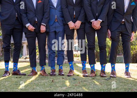 Hommes debout dans une rangée avec leur pantalon levé pour révéler leurs chaussettes lors d'un mariage Banque D'Images