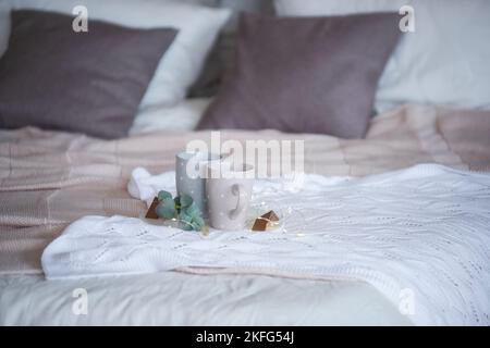 Sur un tissu tricoté, texturé, blanc, se trouve un plateau rond en marbre avec une branche d'eucalyptus vert, sur lequel il y a deux tasses grises avec des points de polka. Acquisition Banque D'Images