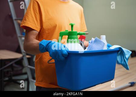 Personne dans une chemise lumineuse portant une boîte avec des produits de nettoyage Banque D'Images