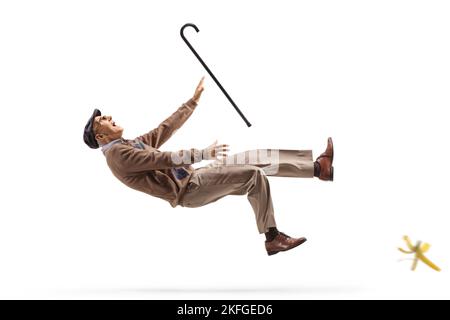 Homme âgé avec une canne de marche glissant sur la peau de banane isolée sur fond blanc Banque D'Images