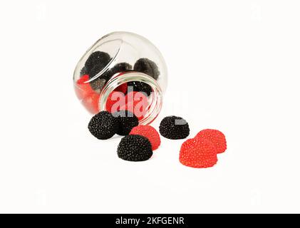 Des gelées sucrées de jus de fruits rouges et noirs sous forme de mûres et de framboises déversées d'un pot. Banque D'Images