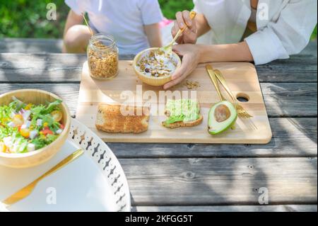 Crop femme et enfant manger petit déjeuner sain dans le parc Banque D'Images