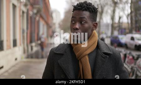 Jeune homme noir élégant marchant dans le trottoir pendant la saison d'hiver à explorer la ville ou les transports en commun Banque D'Images