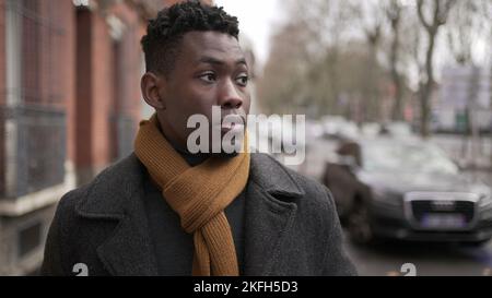 Jeune homme noir élégant marchant dans le trottoir pendant la saison d'hiver à explorer la ville ou les transports en commun Banque D'Images