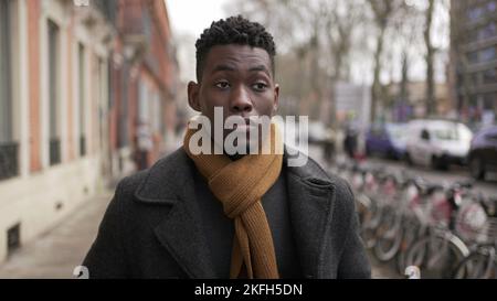 Jeune homme noir élégant marchant dans le trottoir pendant la saison d'hiver à explorer la ville ou les transports en commun Banque D'Images