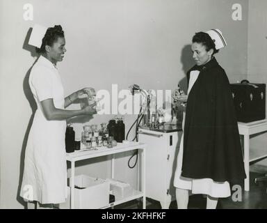 Capitaine Mary L. Petty, infirmière en chef, tenant une bouteille de verre et la montrant au 2nd Lieutenant Olive Bishop, qui écrit sur un petit bloc de papier, 1939 - 1945. Banque D'Images