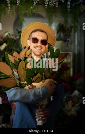 Attrayant race de race blanche dans des lunettes de soleil et chapeau tenant grand bouquet de fleurs de printemps frais dans le magasin de fleurs. Concept de la Fête des mères, de la Saint-Valentin ou de la Journée internationale de la femme Banque D'Images