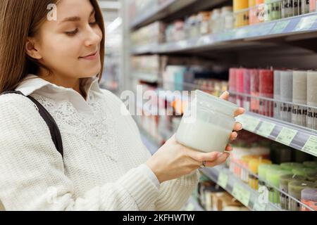 Jeune femme sentant une bougie parfumée dans un pot en verre en magasin Banque D'Images