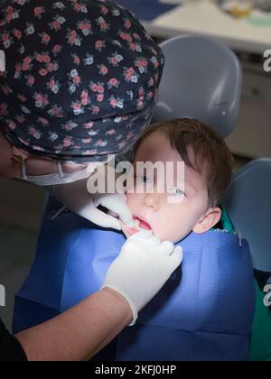 Vue en grand angle d'une femme dentiste portant une casquette florale et des gants chirurgicaux examinant les dents d'un garçon à l'hôpital Banque D'Images