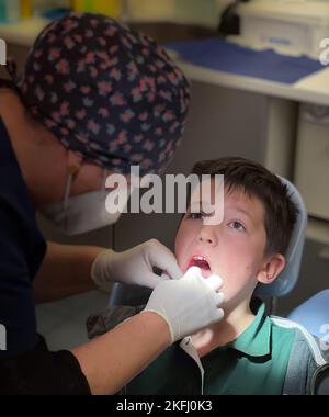 Femme dentiste portant une casquette florale examinant les dents d'un adolescent assis sur une chaise dans une clinique dentaire Banque D'Images